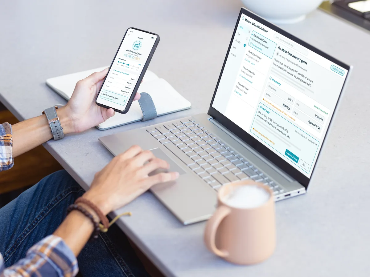 A phone showing an AI-maintained account record beside a laptop with the AI-assisted email workspace